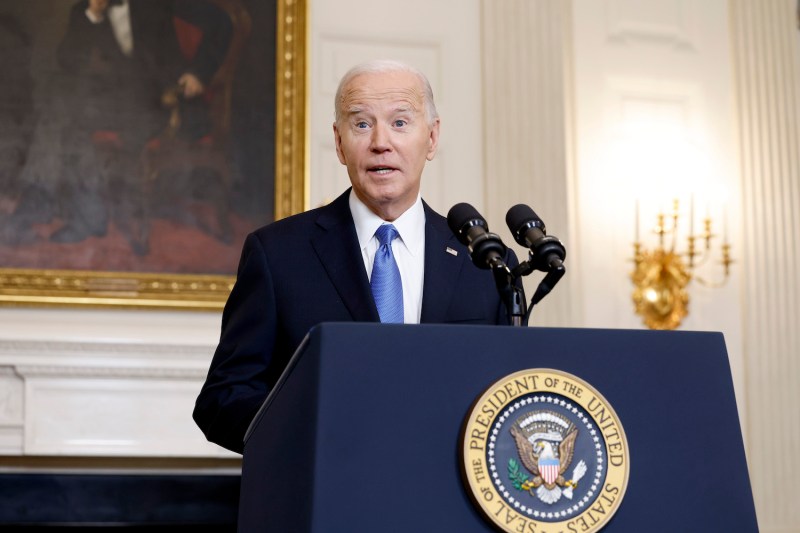 U.S. President Joe Biden speaks at a podium in the State Dining Room of the White House. The seal of the United States is affixed to the podium, and a gold-framed portrait of Abraham Lincoln is visible on the wall behind Biden's shoulder.