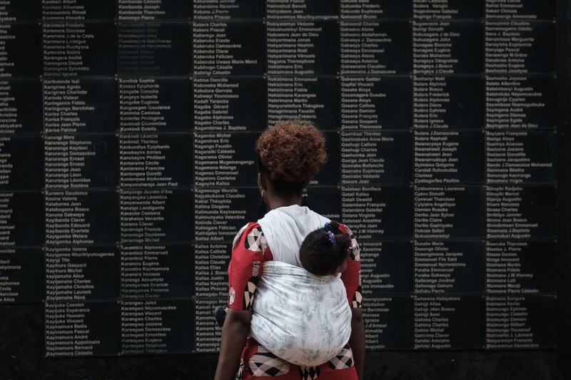 A woman stands in front of a wall of victims' names at a memorial for the 1994 Rwandan genocide.