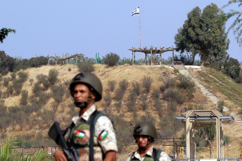 Jordanian soldiers stand guard near the “Gate of Peace” at the Jordan Valley site of Baqura, east of the Jordan River, with the Israeli flag flying over the Israeli side of the border.