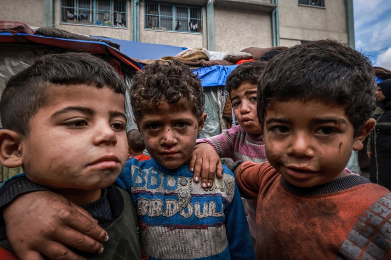 Displaced Palestinian children pose for photos standing in front of makeshift tents at a camp beside a street in Rafah.