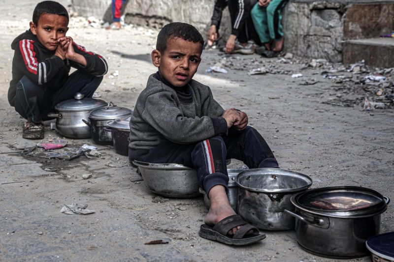 Two boys sit with empty pots as they queue for aid.