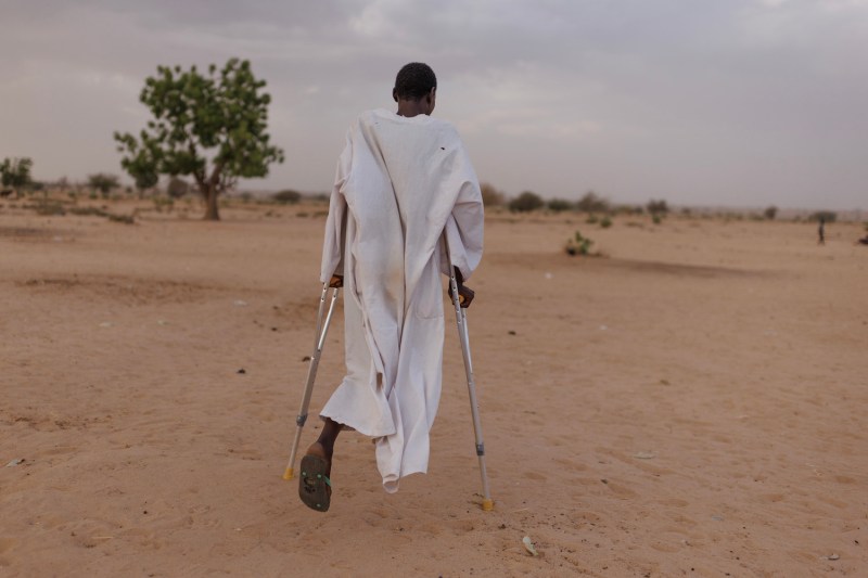Ishag Abdullah Khatir, 30 from Geneina in West Sudan whose leg was amputated after he was shot by RSF soldiers, walks through Ambelia refugee camp on April 20 in Adre, Chad.