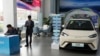 FILE - Sales staff stand near the Seagull electric vehicle by Chinese automaker BYD at a showroom in Beijing, April 10, 2024.