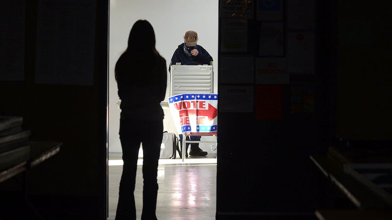 FILE - A first-time voter waits in the doorway for a voting booth as another voter completes...