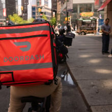 Delivery driver on bike wearing Doordash backpack riding through city