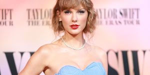 taylor swift looks at the camera, she wears a powder blue dress and pearl necklace, she stands with one hand on her hip