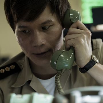 actor hoa xuande holding a cord phone to his left ear with a concerned look on his face in a scene from the sympathizer