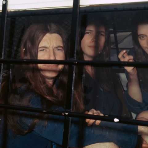 three female members of the manson family sit inside a police vehicle with cars on the window