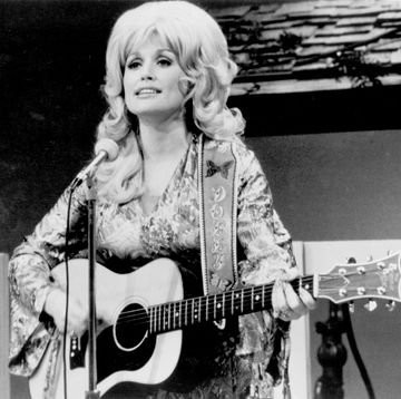 dolly parton playing guitar in front of a microphone and looking off into a crowd