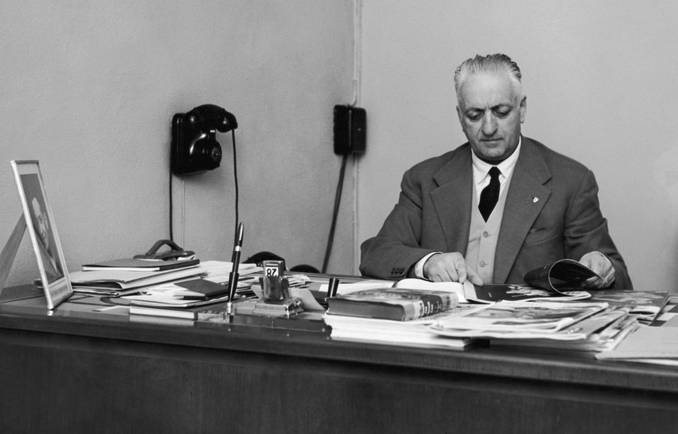 enzo ferrari looking through items while sitting at his office desk