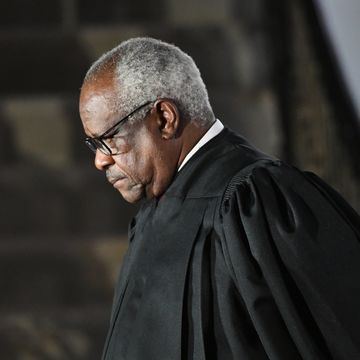 supreme court justice clarence thomas, seen in profile, is standing while wearing his black justice robes and black glasses, he is looking down with a neutral expression on his face