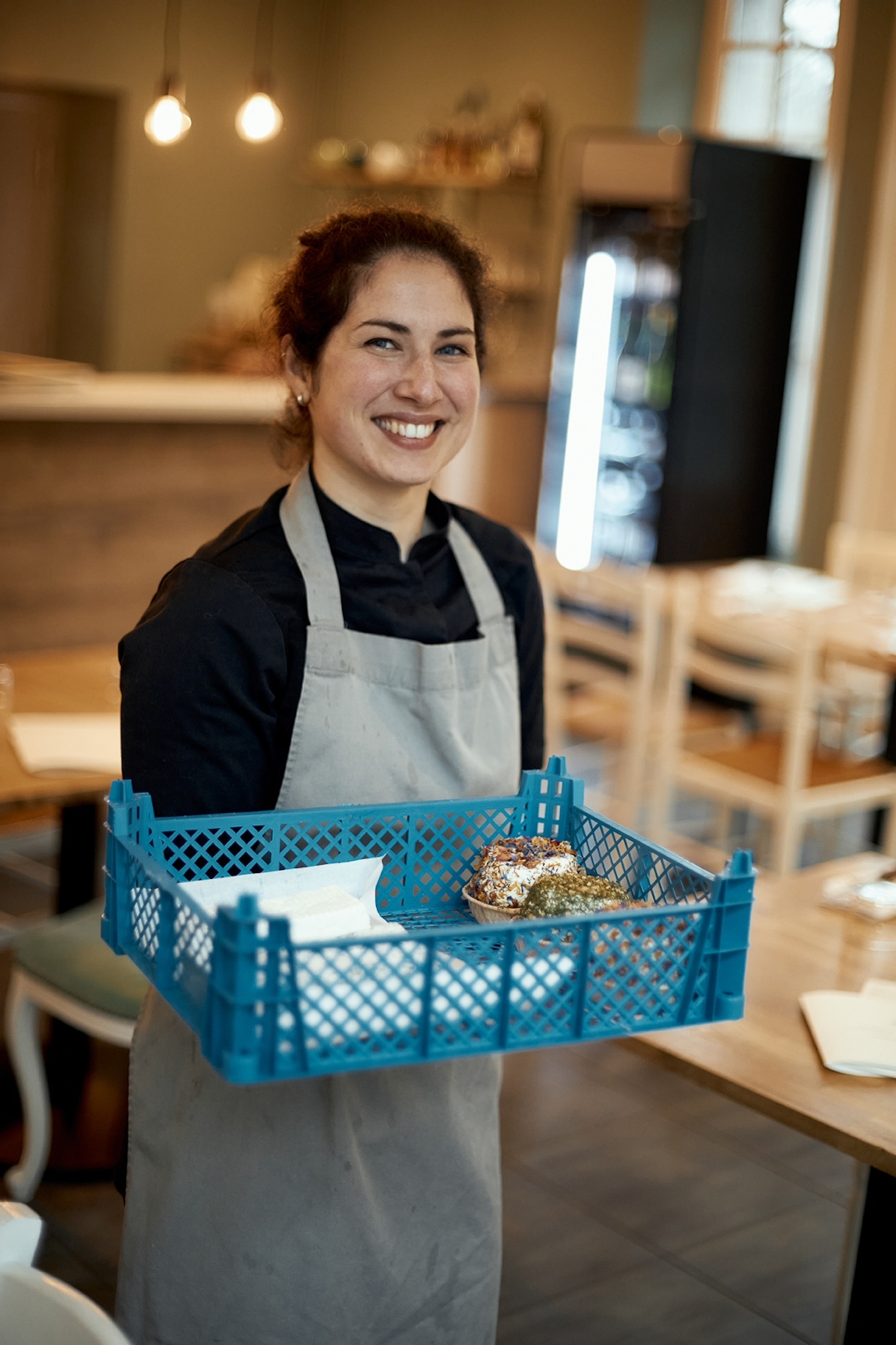 A female chef holding a crate of fresh produce and smiling.