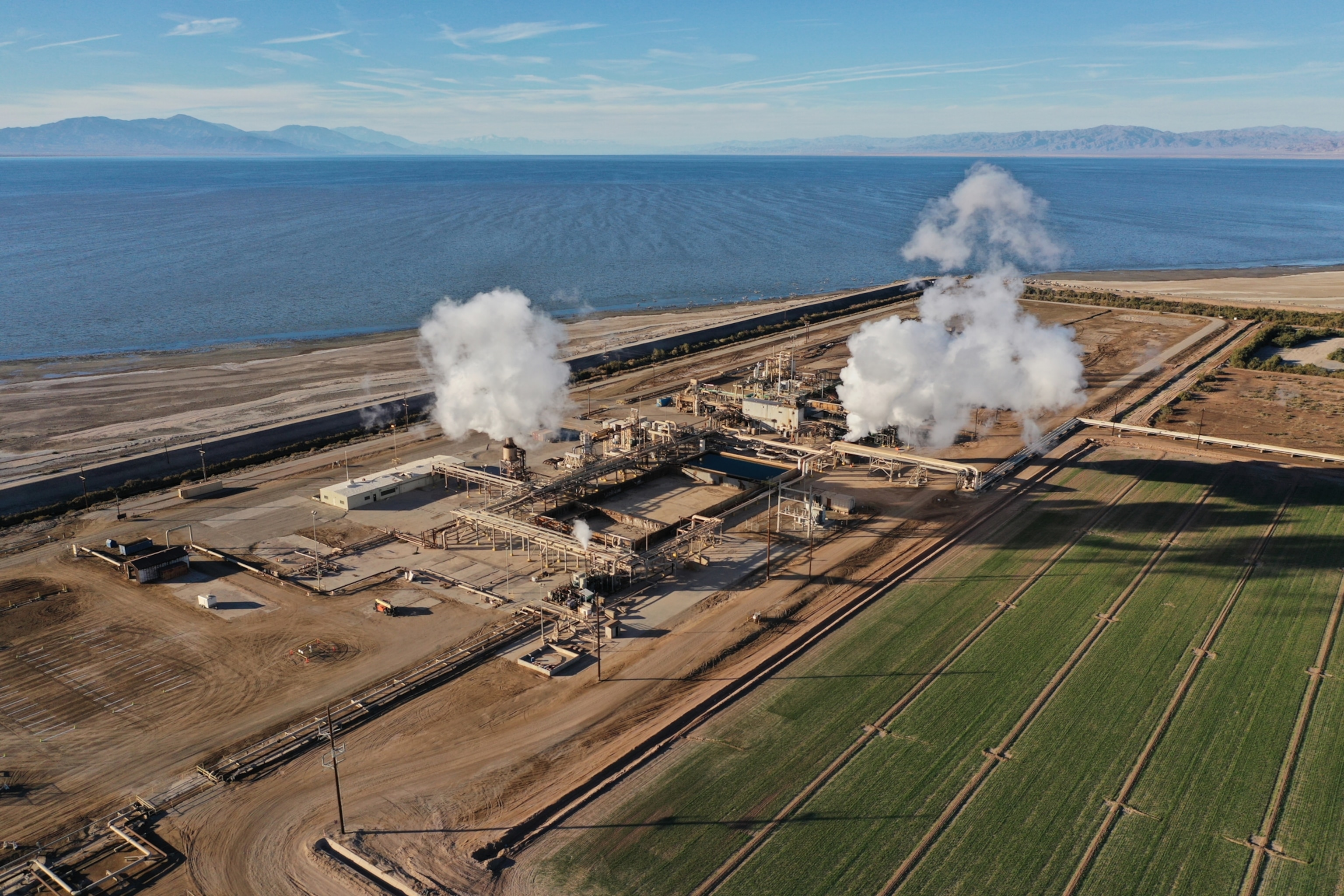 steam rises from a geothermal power plant situated next to a large body of water