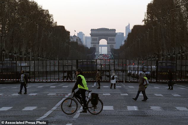 A yellow vest protestor rides a bicycle as police officers block with a fence the access of the Champs Elysee avenue on Place of Concorde during a demonstration called by the CGT (General Working Confederation) union, Tuesday, Feb. 5, 2019 in Paris. Workers, public servants, and retired people were invited to march during a strike called by the CGT. (AP Photo/Michel Euler)