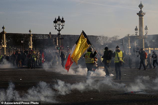 Yellow vest protestors holding a French flag with a yellow banner stand in tear gas during a demonstration called by the CGT (General Working Confederation) union, Tuesday, Feb. 5, 2019 in Paris. Workers, public servants, and retired people were invited to march during a strike called by the CGT. (AP Photo/Michel Euler)
