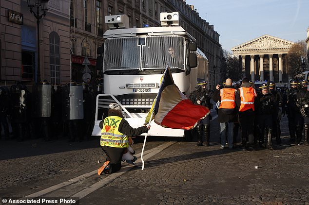 A yellow vest protestor with "Peace" written on the vest and holding a French flag faces a police water canon truck during a demonstration called by the CGT (General Working Confederation) union, Tuesday, Feb. 5, 2019 in Paris. Workers, public servants, and retired people were invited to march during a strike called by the CGT. (AP Photo/Michel Euler)