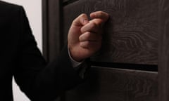 Posed picture, dramatically lit, of a man in a dark suit knocking on a door