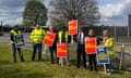 Members of the PCS union hold placards while standing on grass in front of a fence
