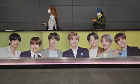 People walk past a commercial poster showing K-pop group BTS