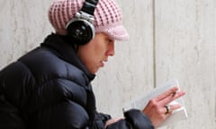 Woman reading a book while listening to headphones.