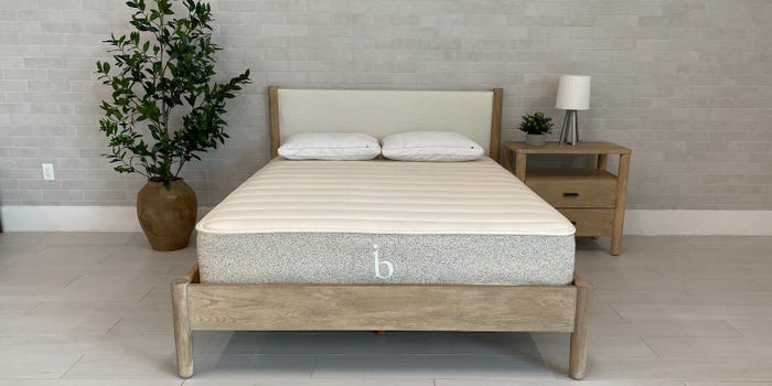The Birch Natural Mattress is displayed on a bed frame in a gray room.