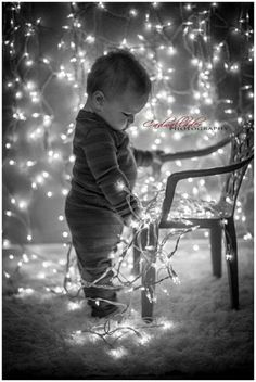 a baby standing next to a chair covered in christmas lights