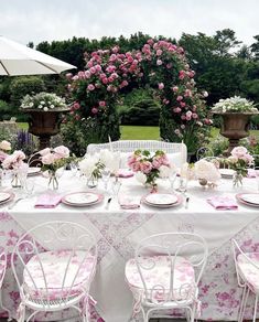 the table is set with pink flowers and white plates for two people to sit at
