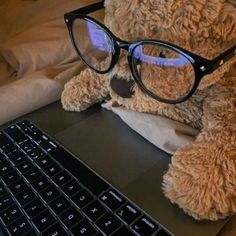 a teddy bear wearing glasses sitting in front of a laptop