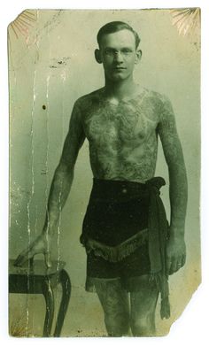 an old photo of a man with tattoos on his chest and arms, holding a chair