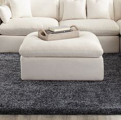 a large white couch sitting on top of a gray rug next to a footstool