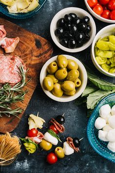 bowls of olives, tomatoes, and meat on a cutting board with other ingredients