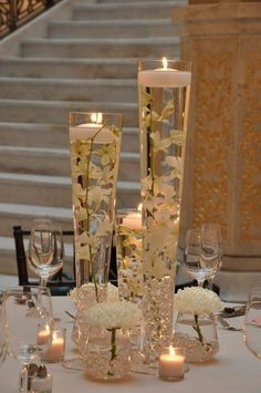 a table with candles and vases filled with white flowers next to some glass wine glasses