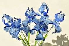 blue glass flowers in a clear vase on a white tablecloth with shadow from the wall behind them