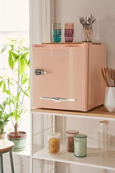 a pink refrigerator sitting on top of a wooden shelf next to a potted plant
