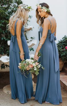 two bridesmaids in blue dresses holding flowers and looking at each other's back