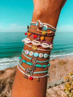 a close up of a person's arm with bracelets on it and the ocean in the background
