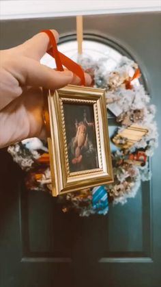 a person holding up a framed photo in front of a door with a wreath on it