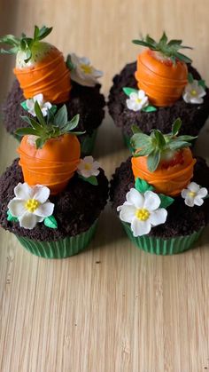 four cupcakes decorated with carrots and flowers on top of a wooden table