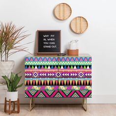 a colorful chest of drawers in a room with two potted plants on the side