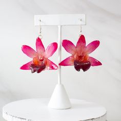 two pink flowers are hanging from earrings on a white stand