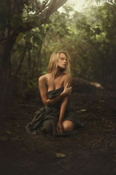a woman sitting in the middle of a forest with her hand on her chest and eyes closed