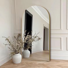 a large mirror sitting on top of a wooden floor next to a vase filled with flowers