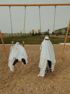 two people in white robes on swings at a park, one wearing sunglasses and the other without