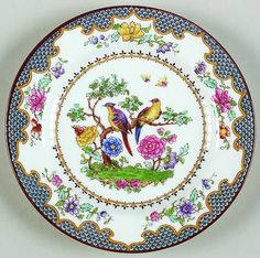 a plate with birds and flowers painted on the front, sitting on a white surface