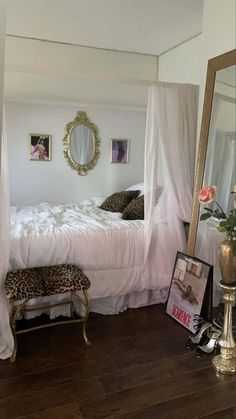 a white bed sitting next to a mirror on top of a wooden floor