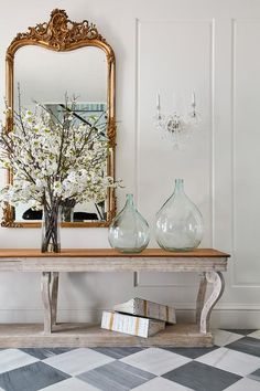 a table with vases and flowers on top of it in front of a mirror