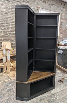 an empty black bookcase sitting on top of a wooden floor next to a brick wall
