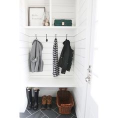 two coats hanging from hooks on a white wall next to a basket and boot boots