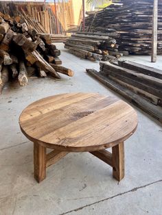 a round wooden table sitting on top of a cement floor next to piles of logs