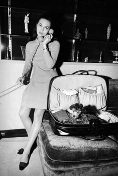 a woman sitting on a couch talking on a phone next to an open suit case